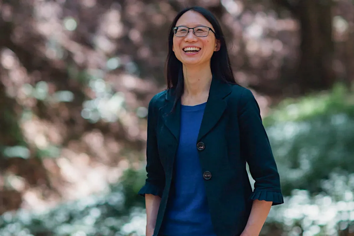 Upside Foods COO Amy Chen stands in an outdoor space, which is out of focus and in the background. She wears a navy blue blazer over a blue shirt.