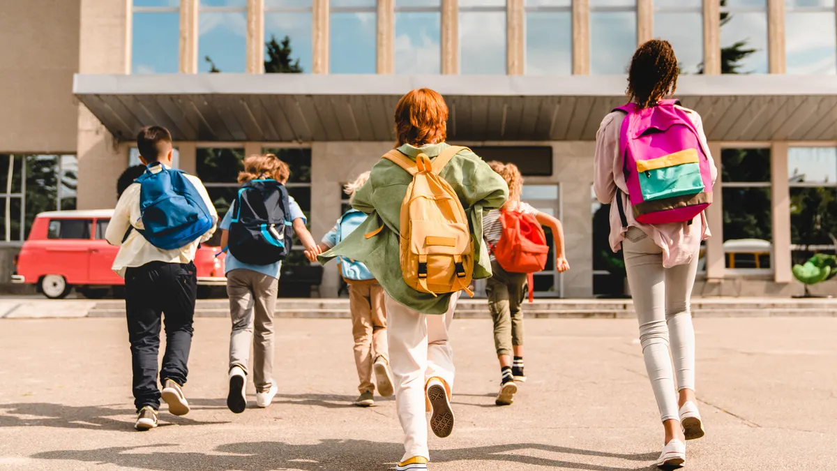 School children with backpacks running toward a school building.