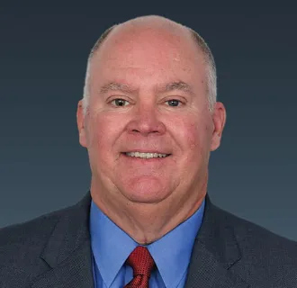 Headshot of a man with thinning white hair and a red tie.