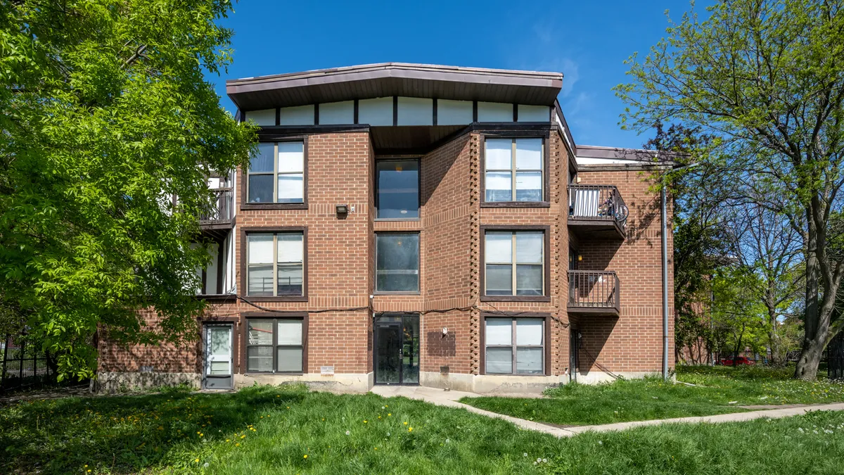 Brick, three-story apartment building with grass and trees in the foreground.