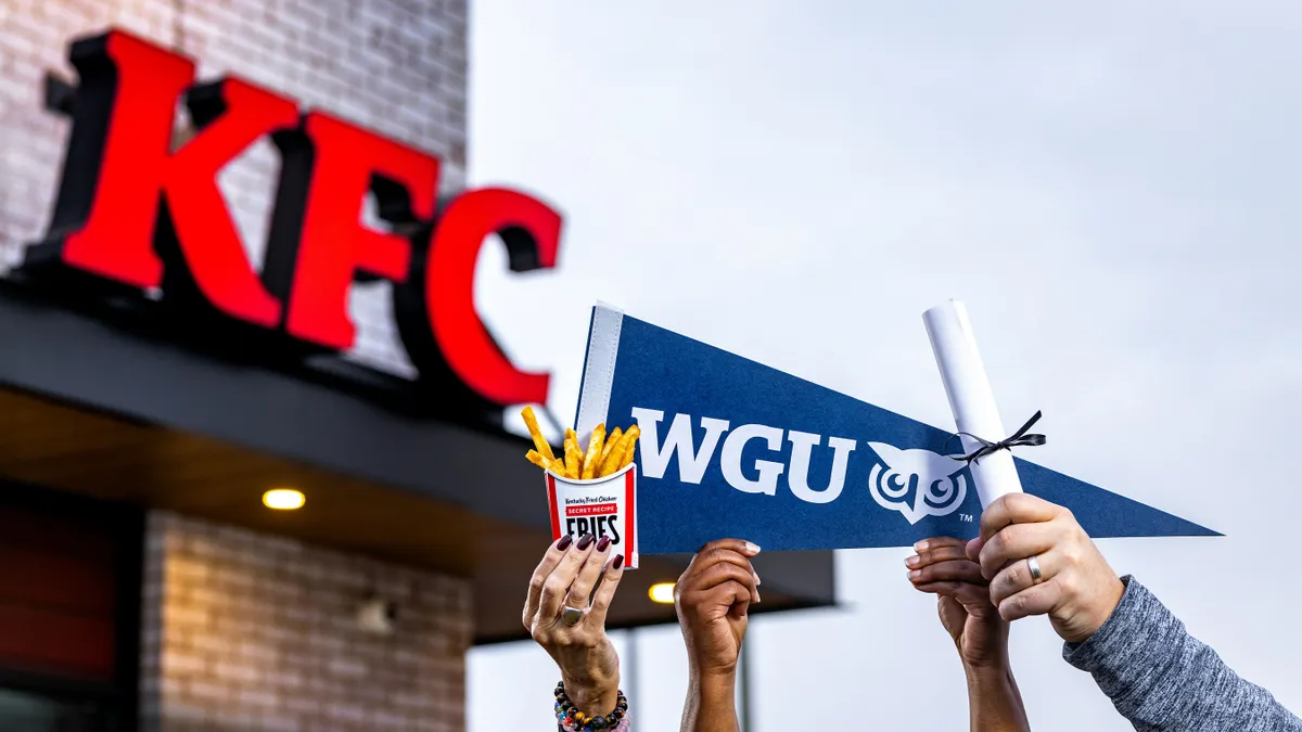 An image of several hands holding KFC products and a WGU pennant in front of a KFC.