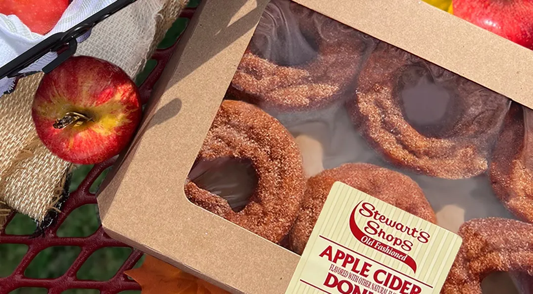A photo of cider donuts from Stewart's Shops surrounded by fall items like apples and orange maple leaves.