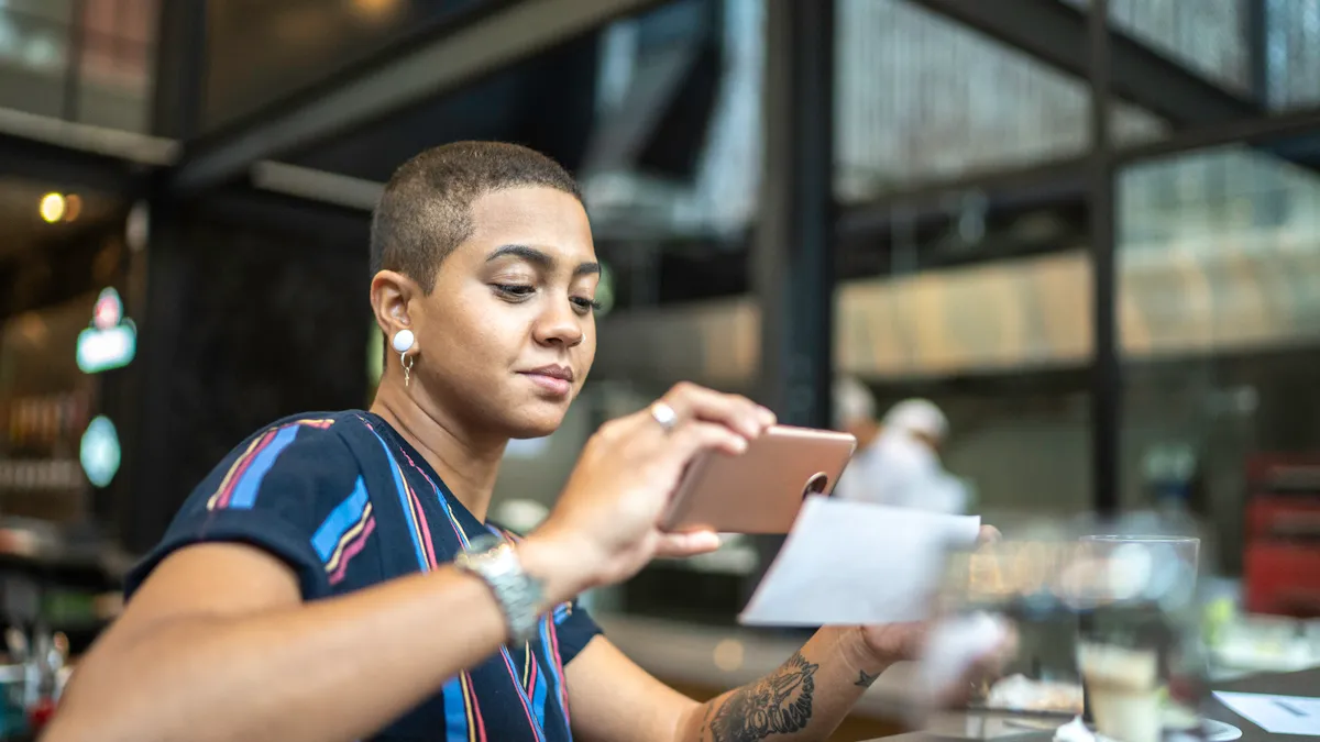 Young woman depositing check by phone in a cafe.