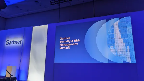 The Gartner logo is displayed on a blue lit-up wall next to a screen that displays the words “Gartner Security & Risk Management Summit”