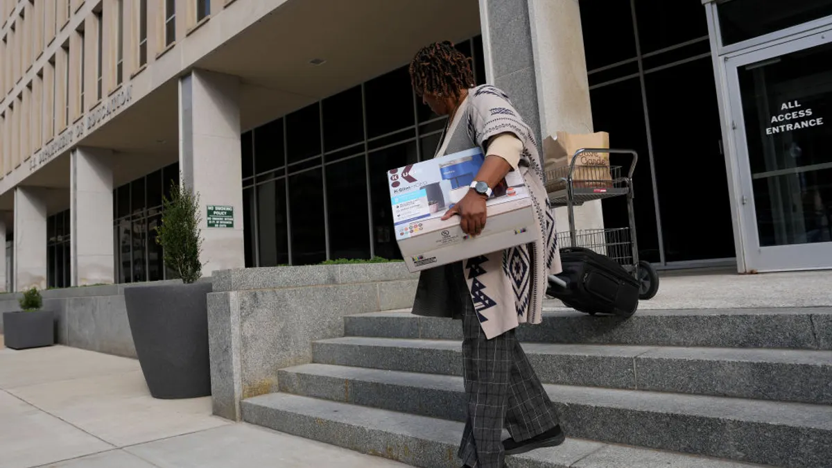 A person is carrying a box while walking down the stairs in front of the outside of a federal building