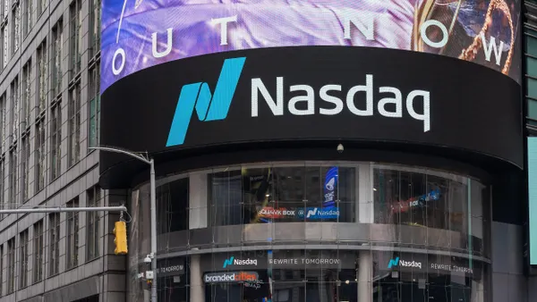 The building features a modern glass façade with the Nasdaq logo prominently displayed. Surrounding the structure are other commercial buildings and digital billboards, which are characteristic of the vibrant Times Square environment.