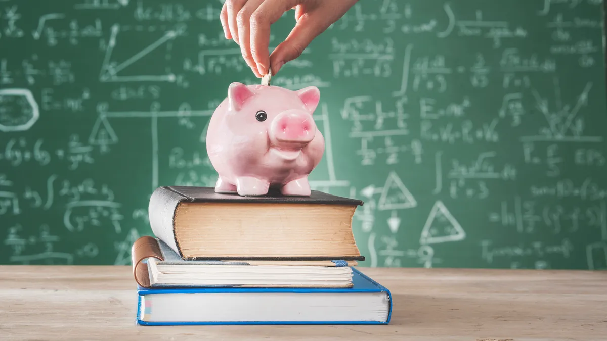 A teacher puts change into a piggy bank in a classroom with a green chalkboard in the background.