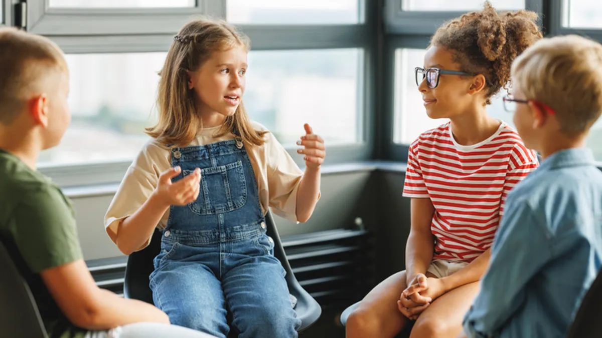 A group of four boy and girl students engages in discussion during class in front of a window.