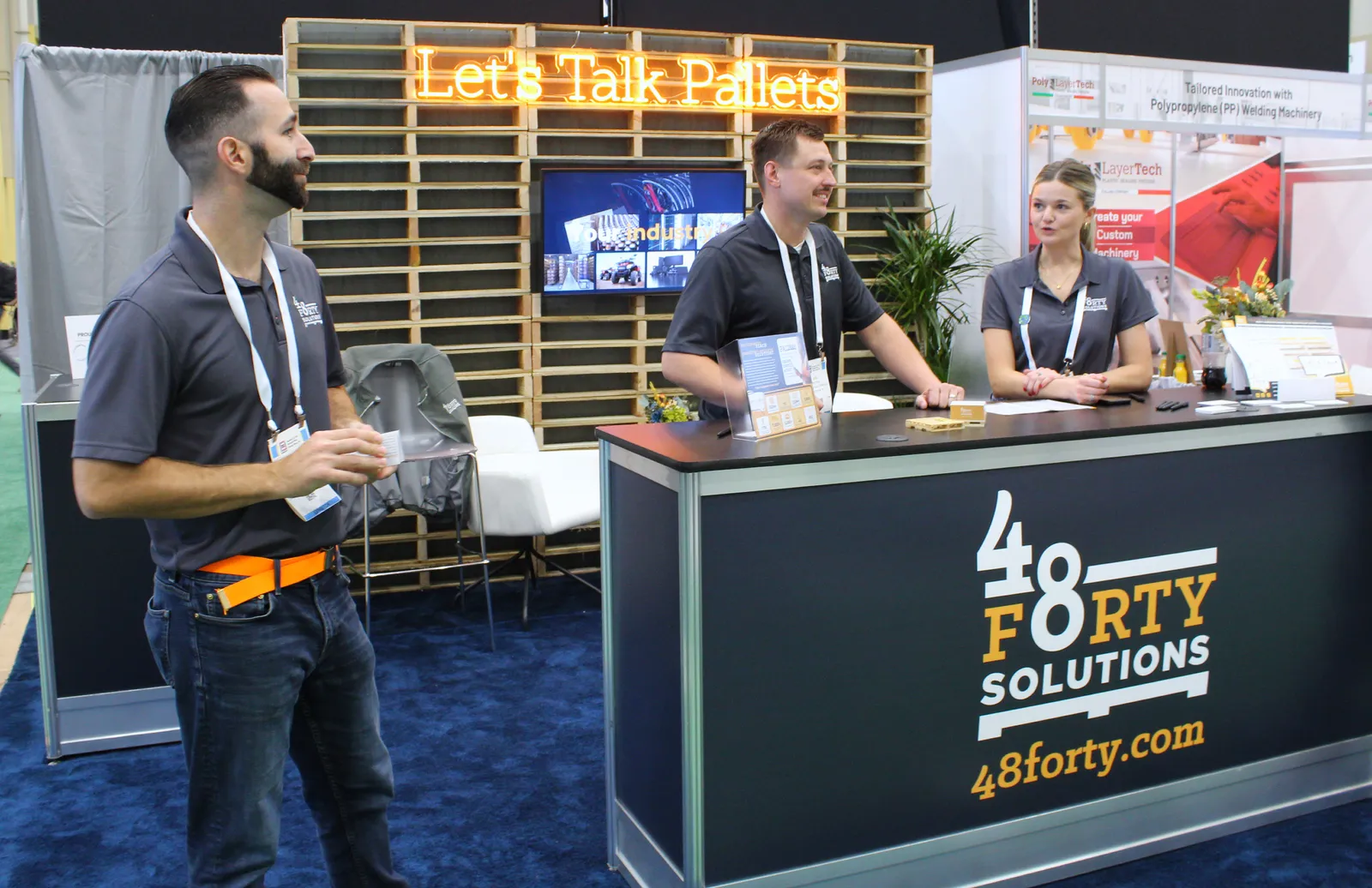 Three people stand in a conference booth for 48forty Solutions.