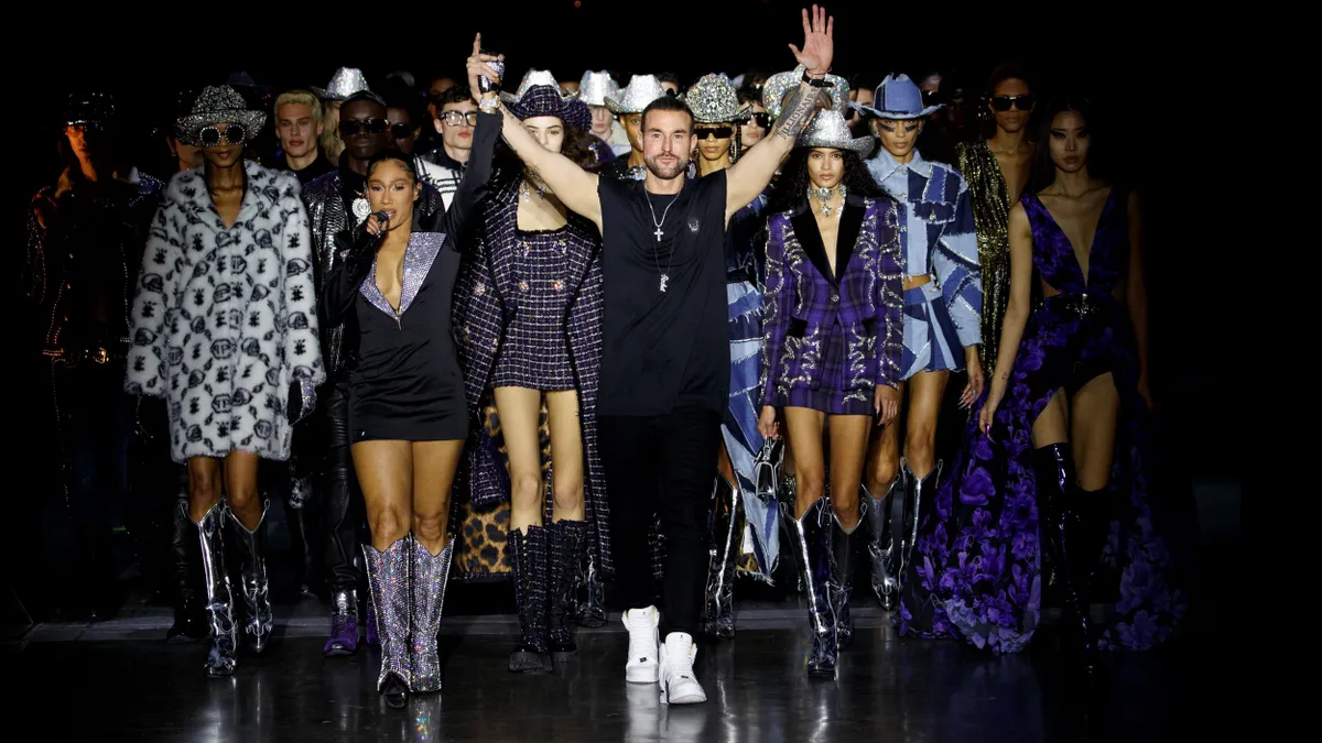 Philipp Plein raises his arms on the runway infront of a group of models wearing clothing from the Philipp Plein brand.