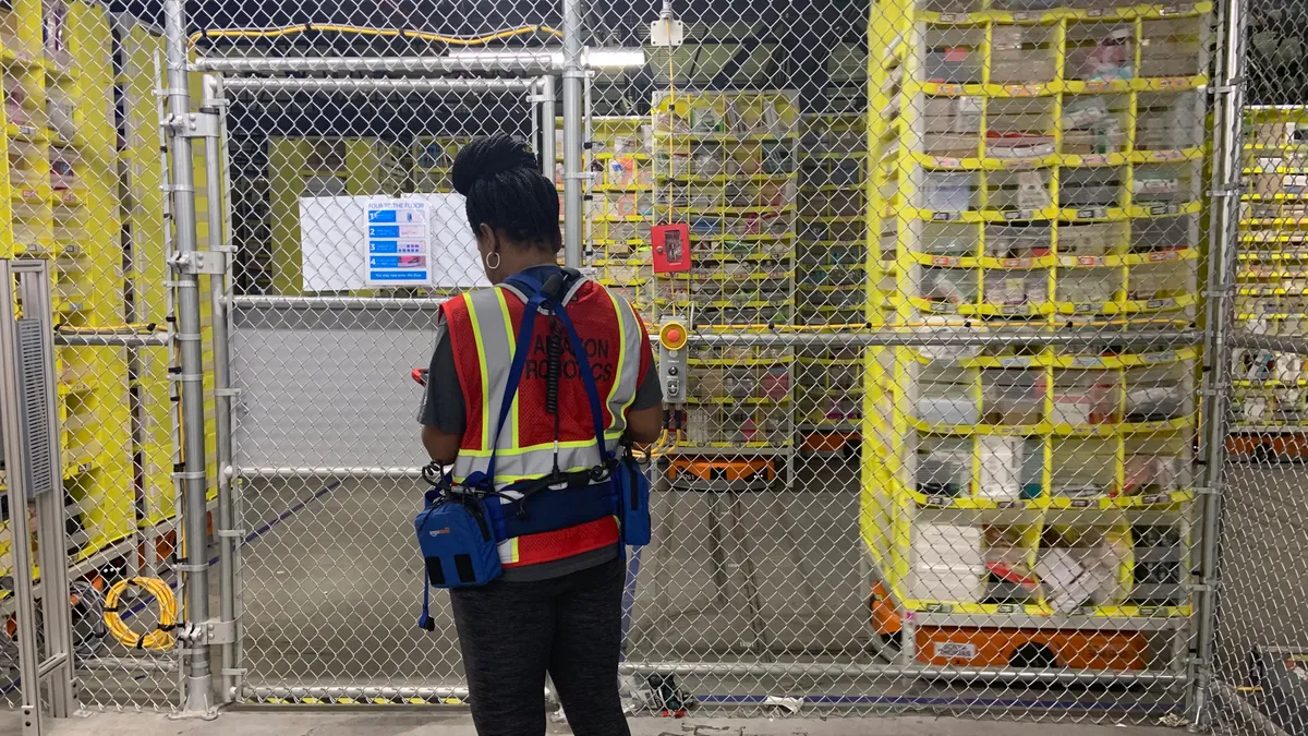 An Amazon Robotics tech consults her tablet outside the cage where robotic "dives" ferry merhcandise around a Staten Island, New York, fulfillment center.