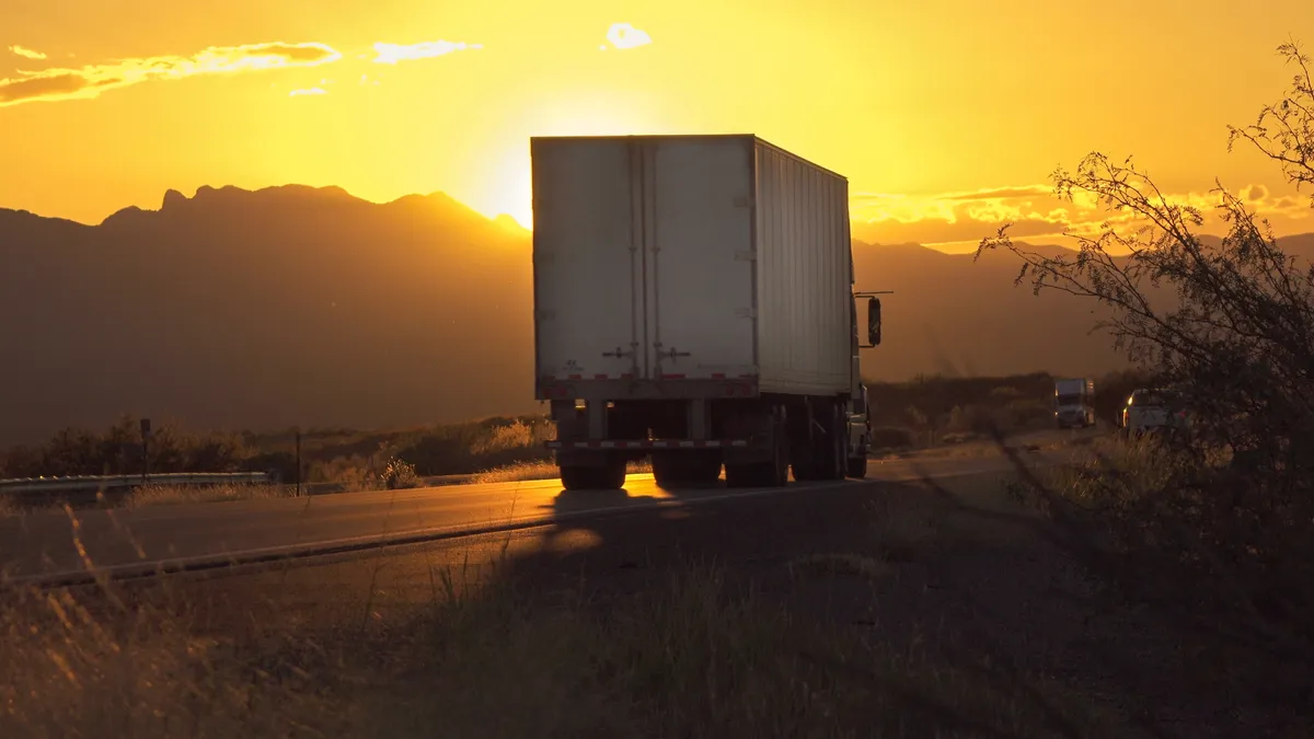 A truck moves along a highway during a summer sunset with a ridge line in the background.