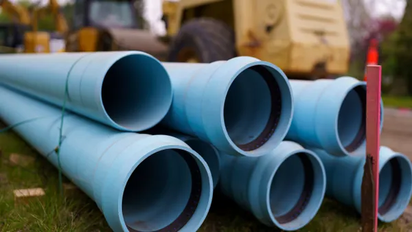 Blue pipes are stacked in front of a yellow bulldozer.