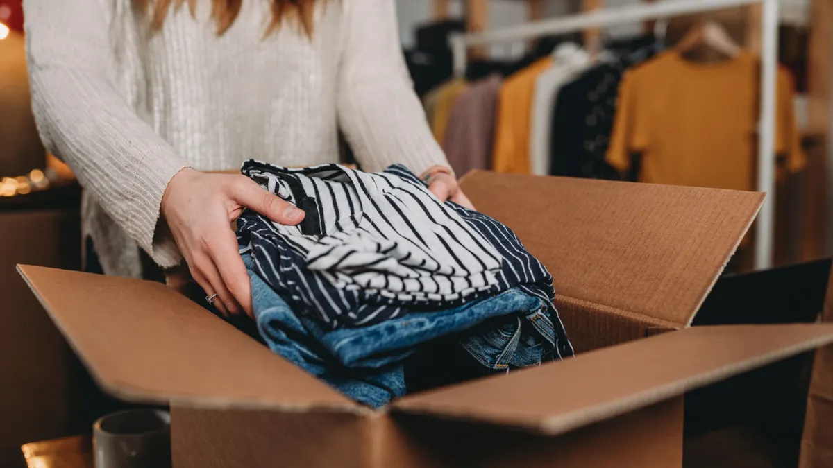 A person puts clothing inside a cardboard box.