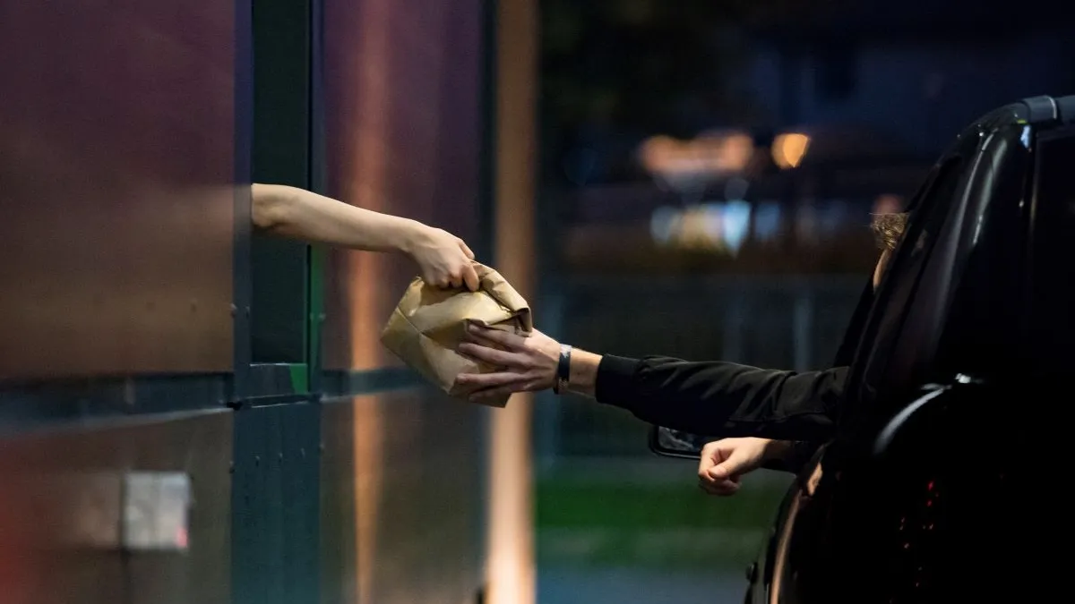 A fast food employee hands a brown bag to a waiting customer in a car.