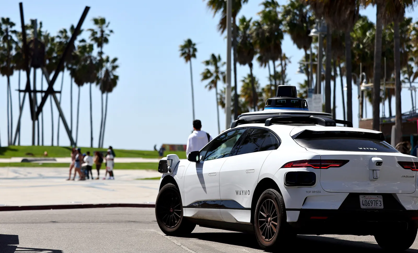 Waymo readies its robotaxis for winter climate 2 A white car labeled Waymo drives among palm trees and people.
