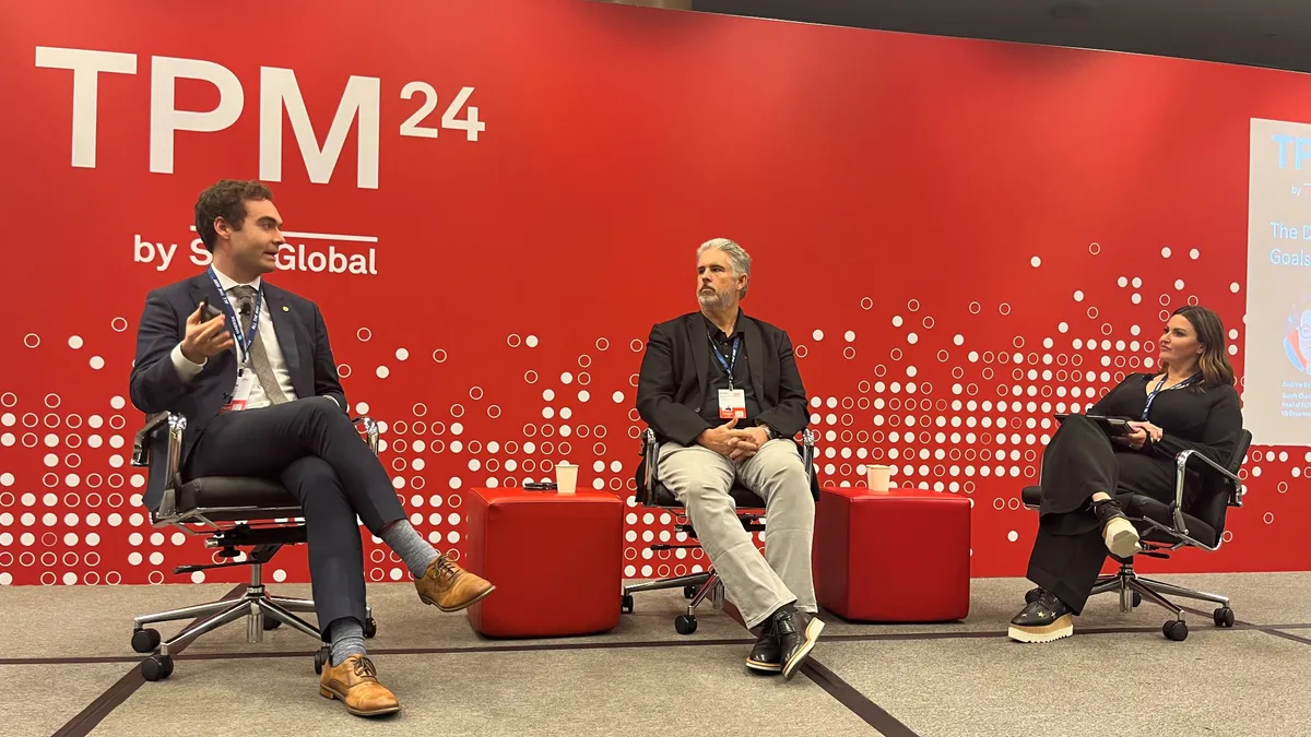 Three people sit on a stage as speakers during a conference panel.