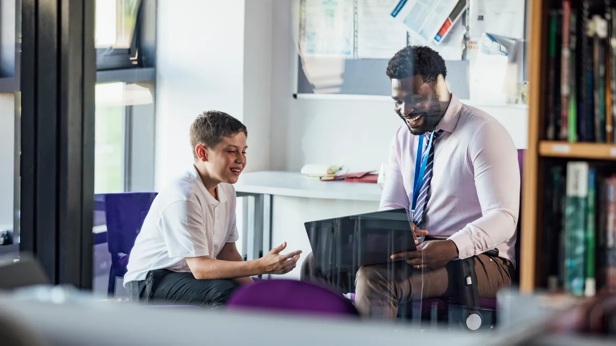 A male secondary school student sitting in an office in the school, having a meeting with his teacher.