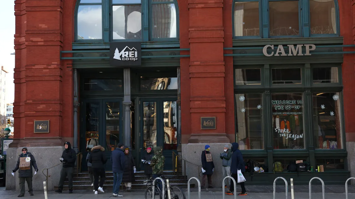 People stand outside a red brick REI store in New York City, with protest signs.