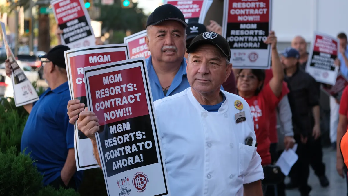 A man holds a picket sign that reads "CONTRACT NOW."