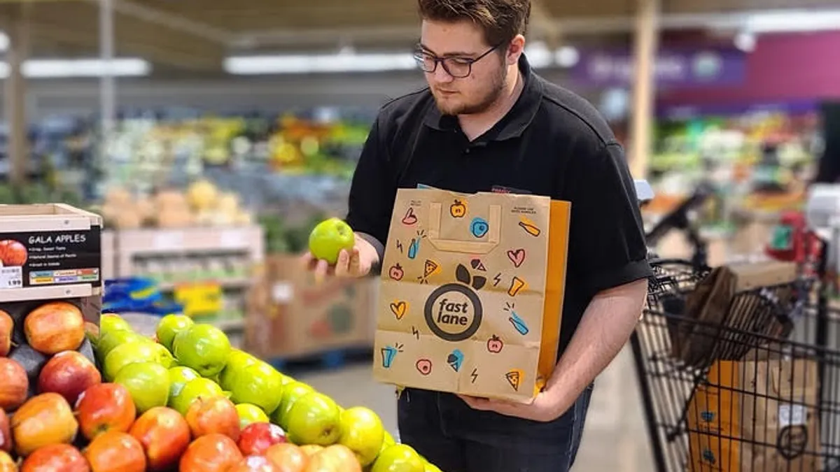 A person holds a bag that says "Fast Lane" in one hand and a green apple in the other hand.