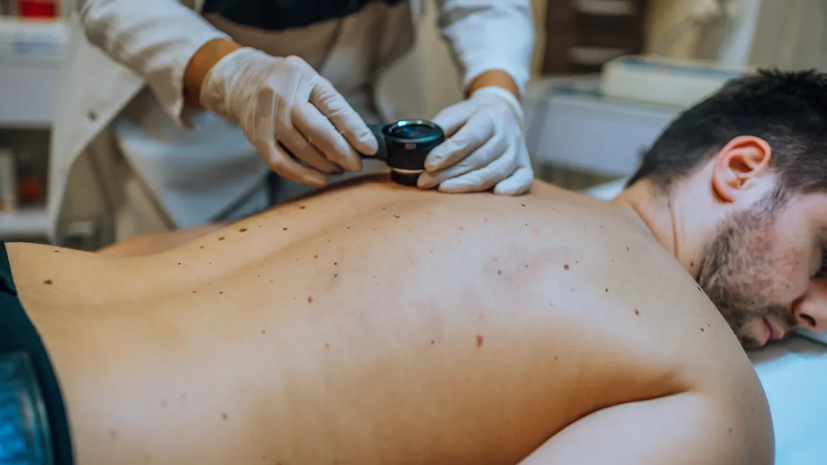 A picture of dermatologist examining patient skin moles with a dermoscope at a health clinic.