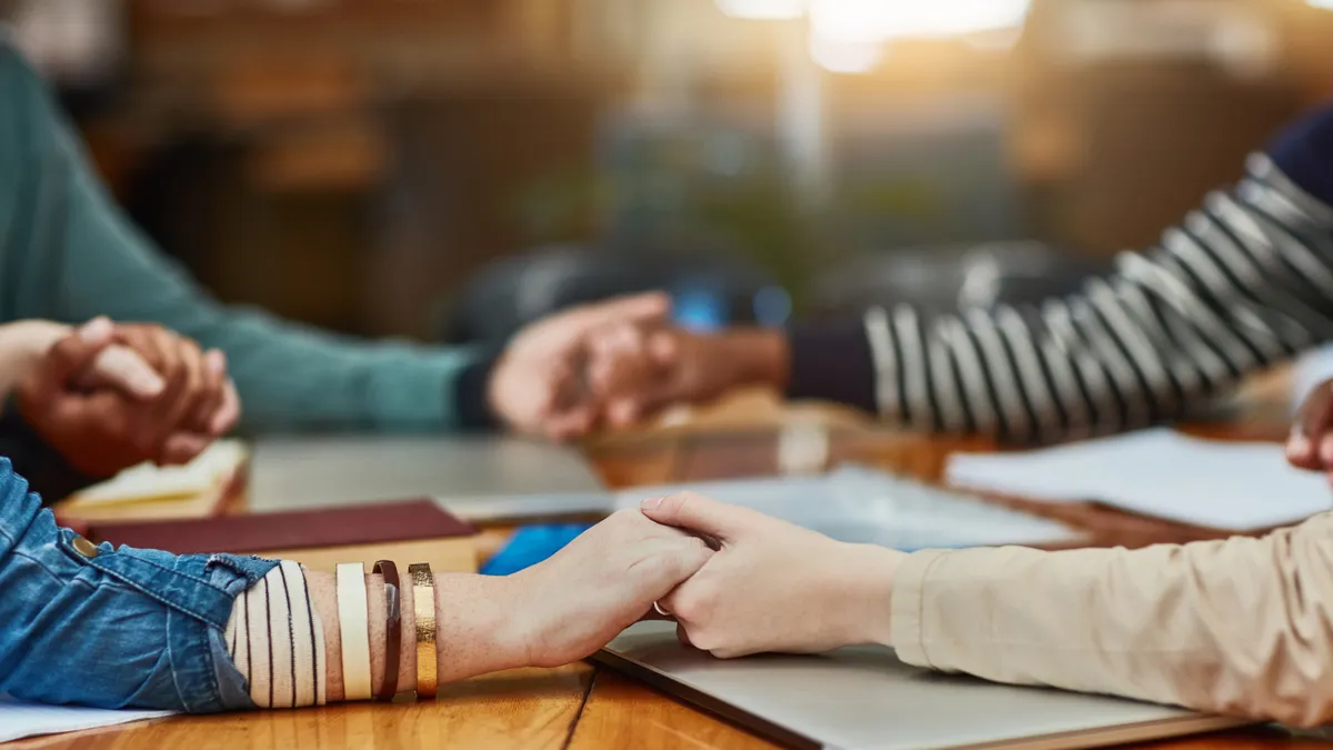 Several unseen people's hands join together to form a circle over top a study hall table.