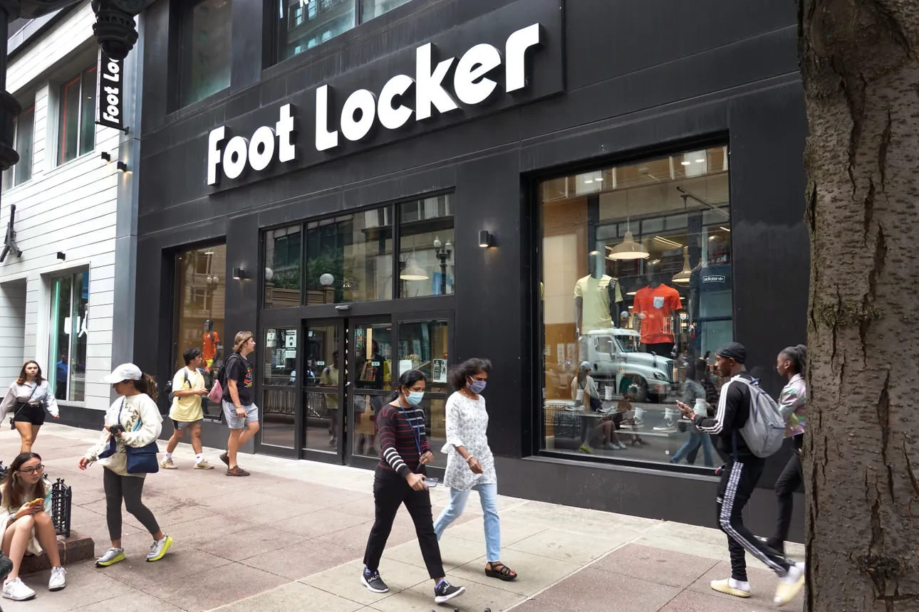 People walk by a Foot Locker store on Aug, 2, 2021 in Chicago. The logo on the outside of the store reads "Foot Locker".