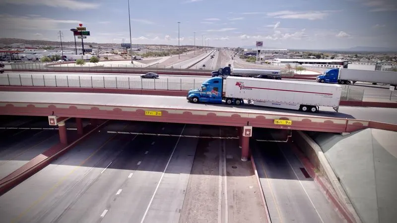 A Mesilla Valley Transportation tractor-trailer crosses on an overpass as nearby traffic also moves.