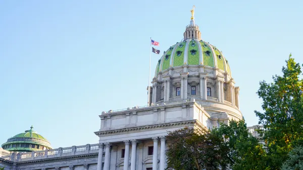 A tall, domed building with a green roof stands in the foreground on a nice day, blue sky and sunny in the evening.