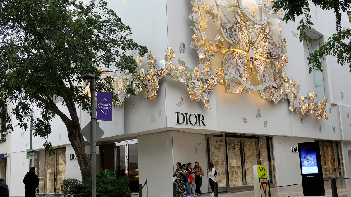 Shoppers wait outside of a Dior storefront.