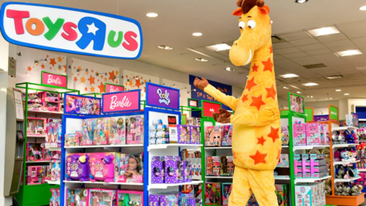 Geoffrey the giraffe points to brightly colored shelves of toys in a Macy's store