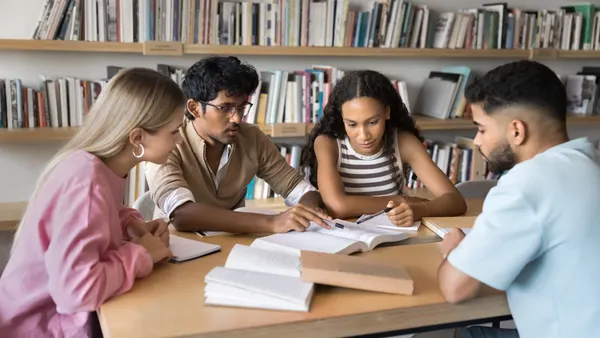 A group of students studies in a library while sitting together at a table.