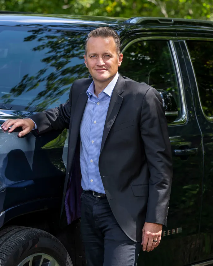 A man in a suit stands near a vehicle