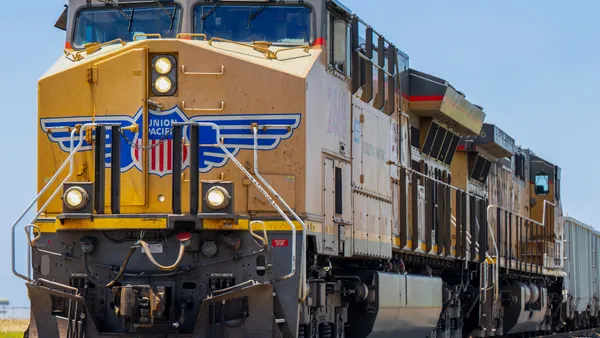 A train with a blue and red logo moves along a train track in front of a blue sky.