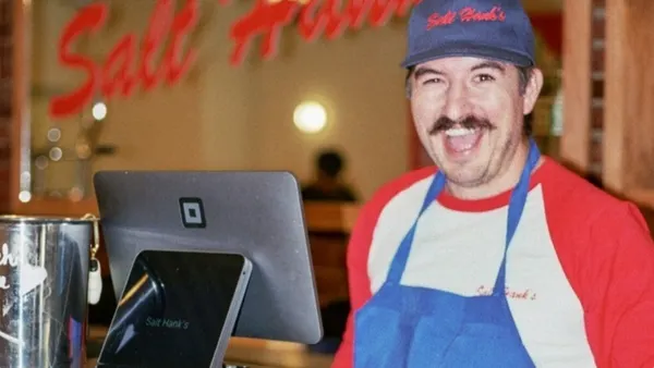 A restaurant worker smiling behind the counter next to a Square kiosk.