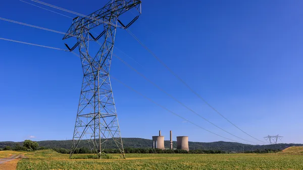 Electric transmission tower and lines cross a field with a power plant in the background.