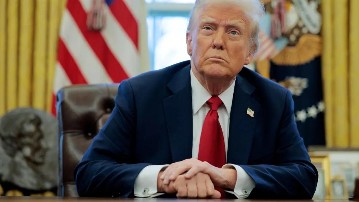 Donald Trump sits at his desk in the Oval Office with his hands clasped.