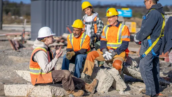 A group of construction workers talk in a circle on a jobsite.