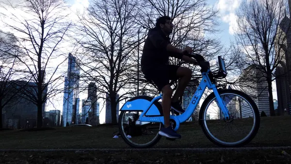 Silhouette of a man riding a blue bike marked "Lyft" and "Divvy" with bare trees and tall buildings in the background.