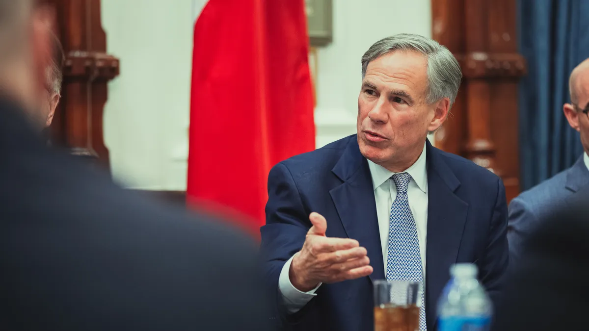 Texas Governor Greg Abbott sits and speaks with his hand raised