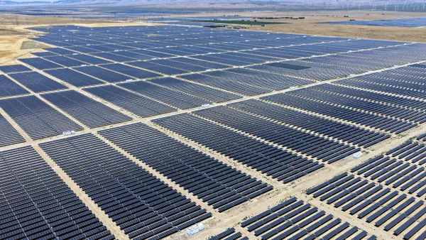 An aerial view of a large solar farm in a desert landscape with mountains in the background