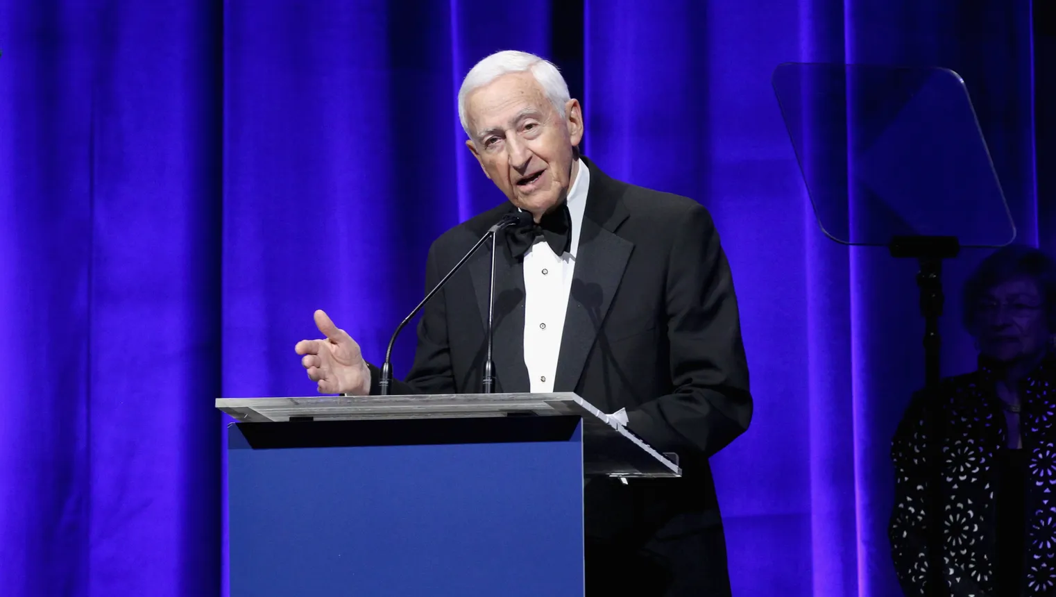 A man dressed in a suit speaks at an event.