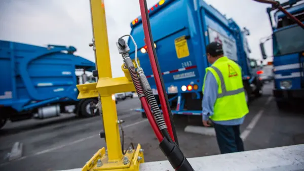 A fuel pump in focus in front of a line of waste trucks.