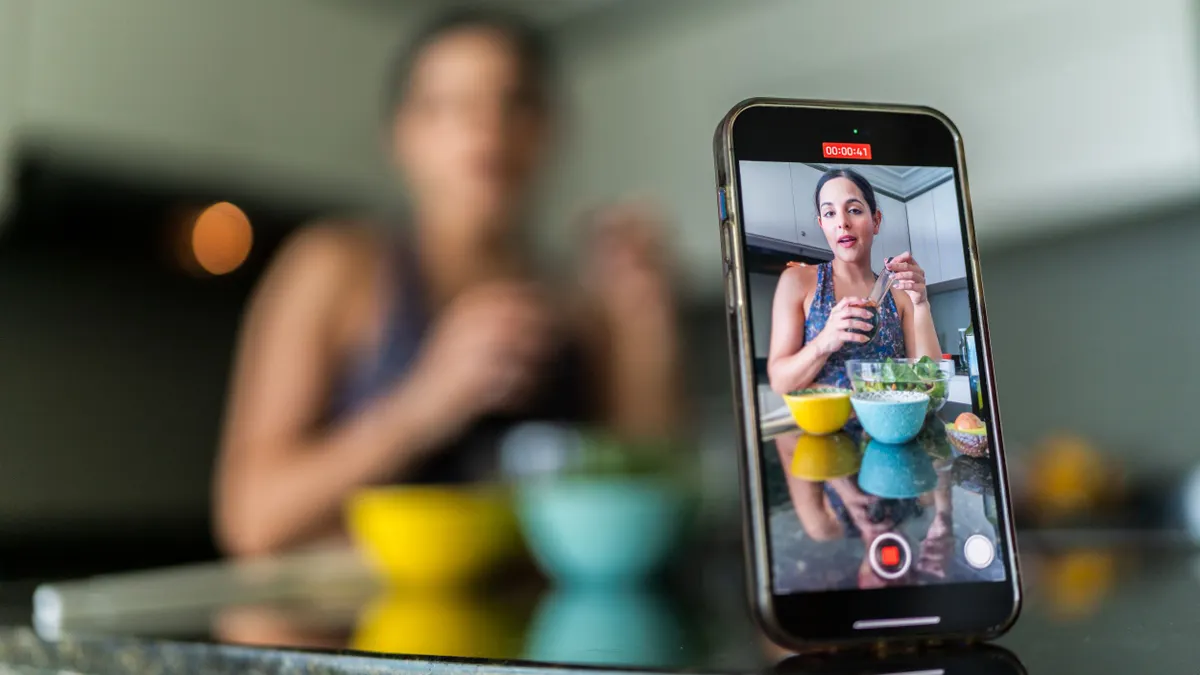 Close-up of a mobile phone recording a young woman vlog preparing salad in kitchen at home