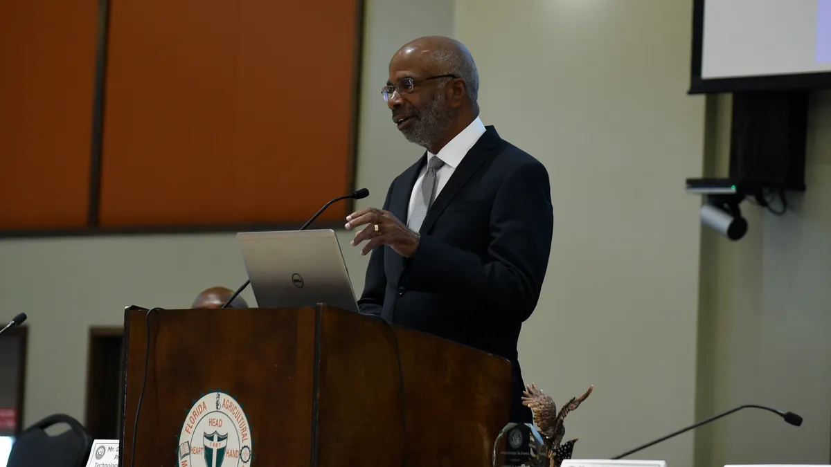 An older Black man speaks at a podium with the FAMU seal on the front.