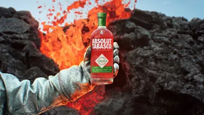 An arm with a glove holding a bottle of Absolut Tabasco vodka in front of a volcano