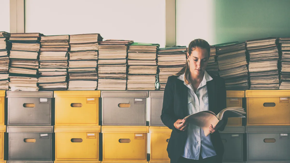 Businesswoman looks over a document file while leaning on a stack of archive boxes.