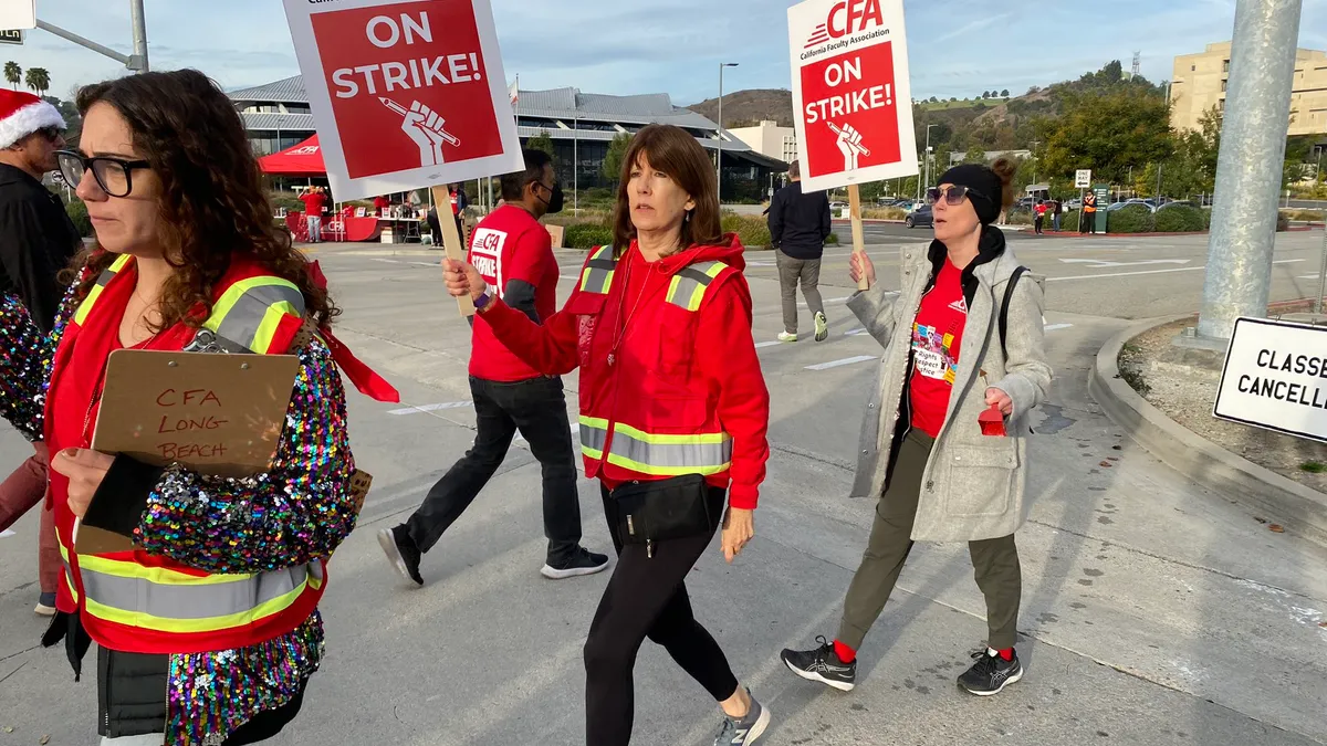 Three people hold up signs as they strike with the California Faculty Association.