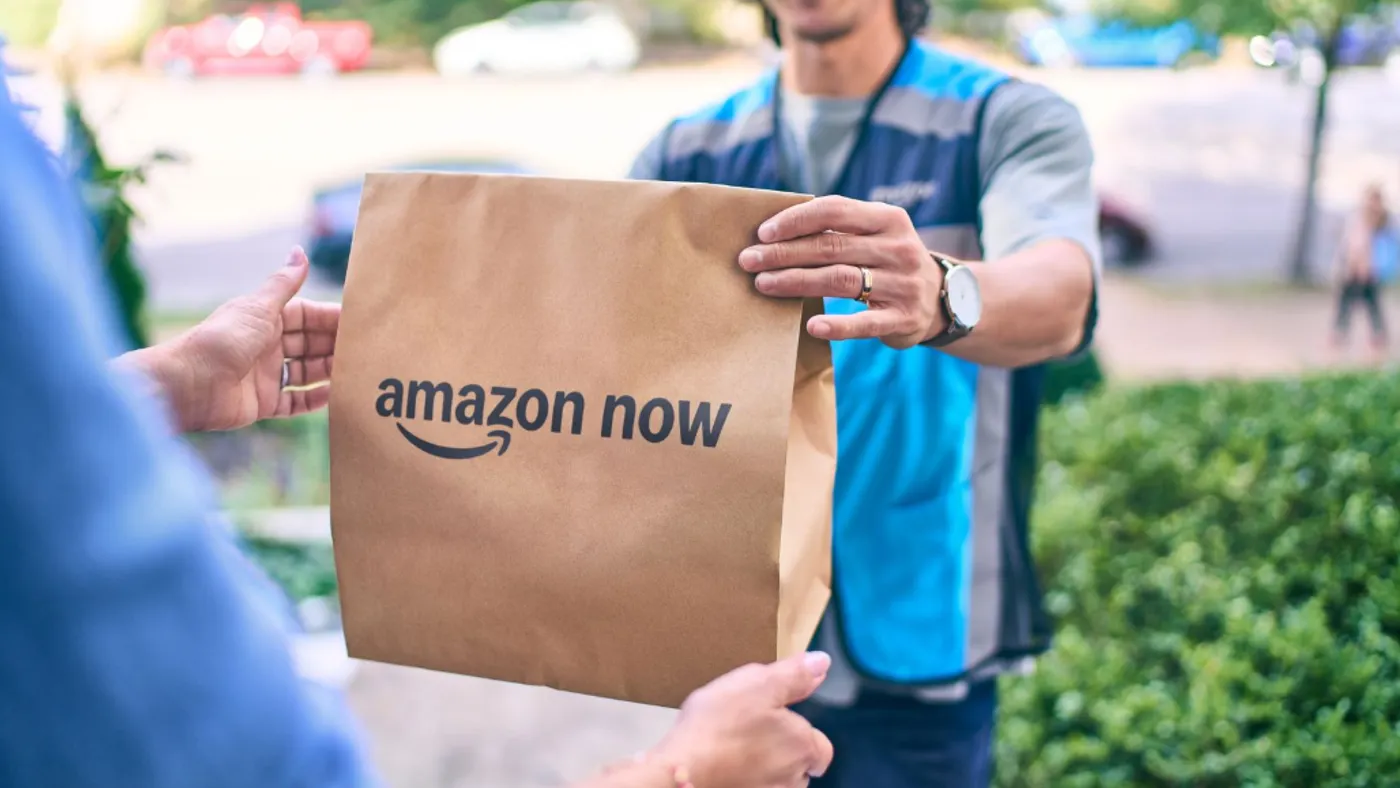 A person hands over a package labeled "Amazon Now."